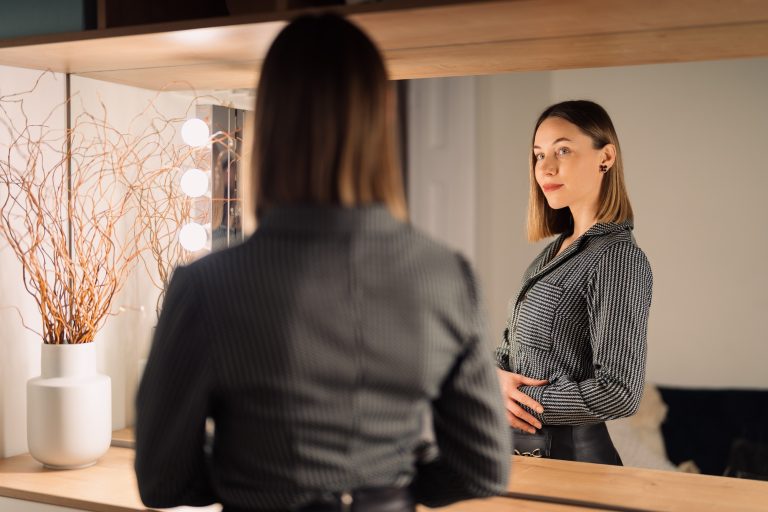 Confident woman looking to her reflection into the mirror